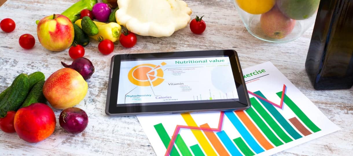 Gesunde Lebensmittel und Tablet mit einer Übersicht der Vitamine